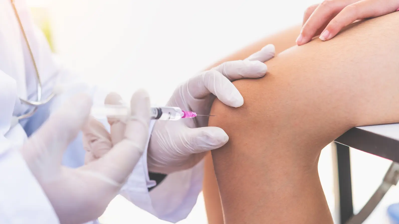 A healthcare professional in gloves administers an injection into a patient's knee. 