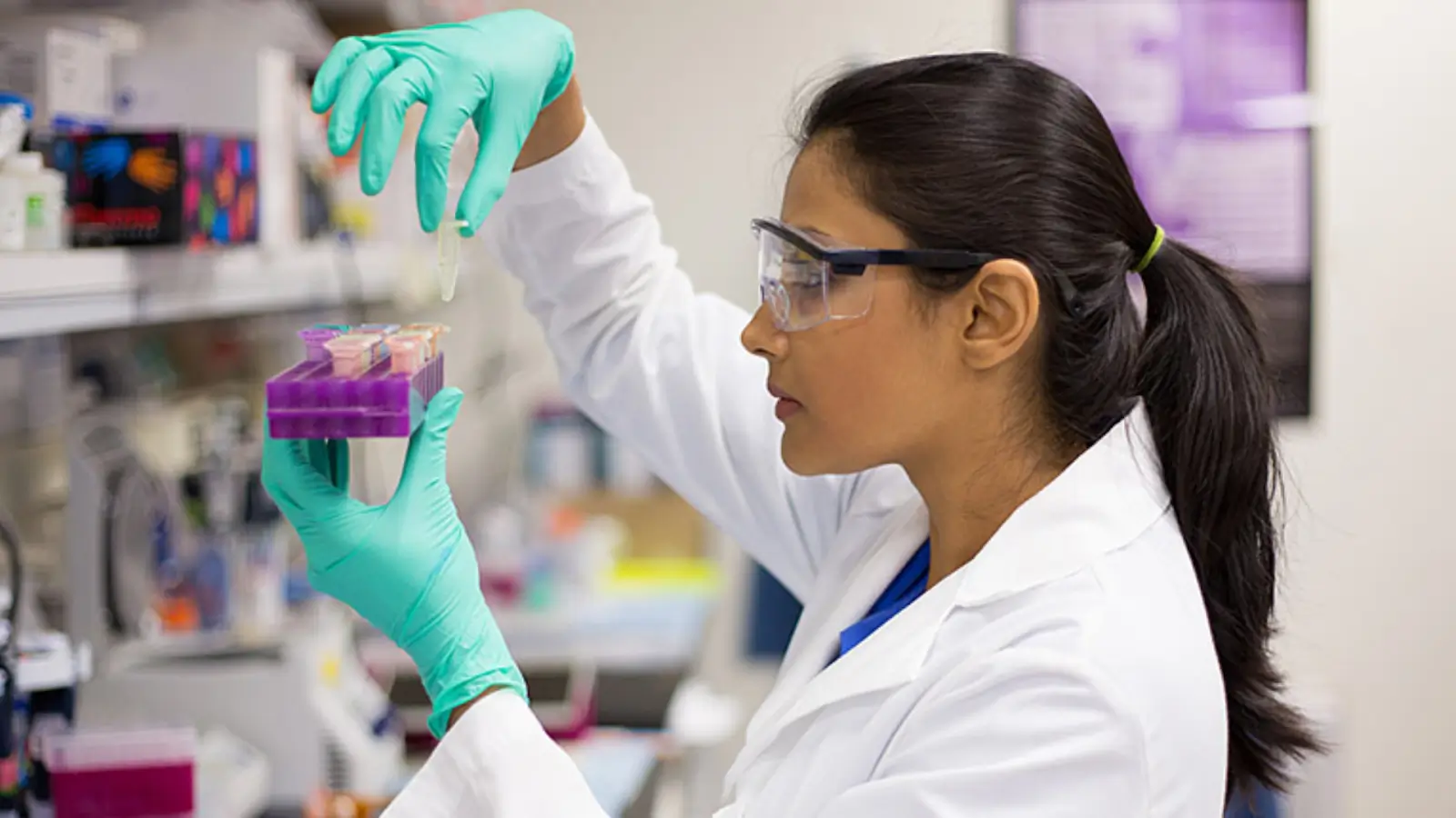 A scientist in a lab coat, goggles, and gloves is carefully pipetting liquid into small tubes in a laboratory setting, perhaps analyzing data related to the Eylea success rate. The background reveals blurred lab equipment and charts.