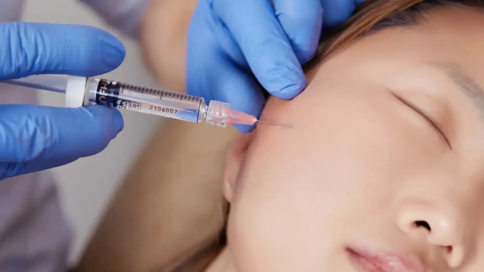 A person receiving an injection in the facial area, administered by someone wearing blue gloves.