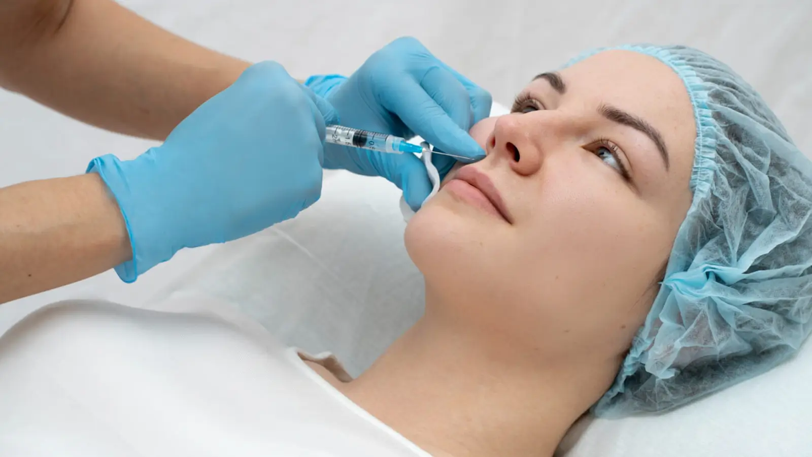 A person lying on a medical table receives an injection for facial rejuvenation.