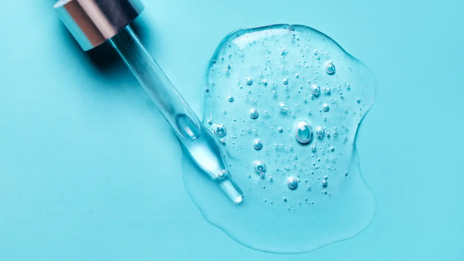 A pipette lays on a blue surface, next to a clear gel-like substance with bubbles. The scene suggests a skincare product or cosmetic formulation.