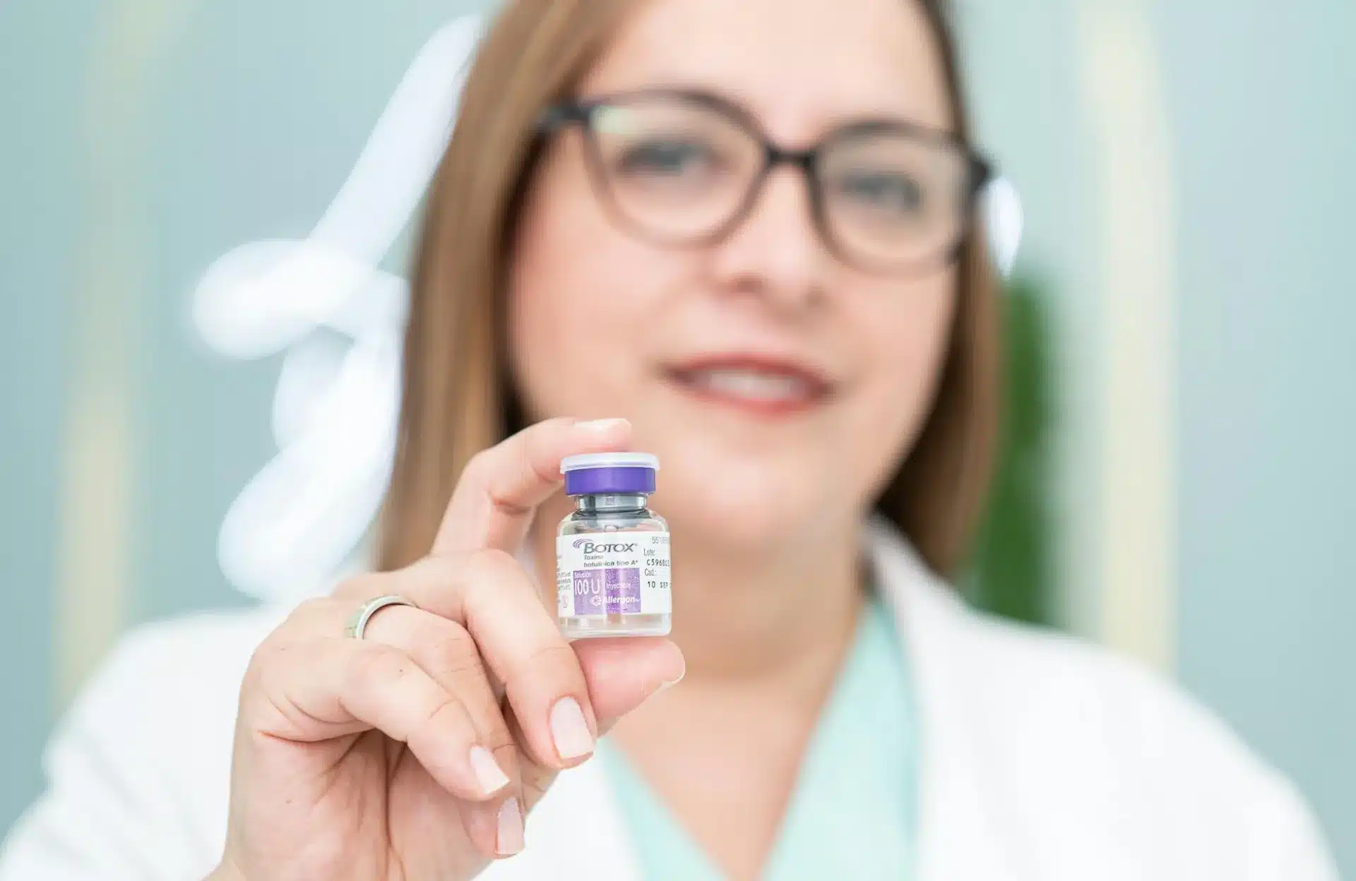 Female doctor with glasses, holding a bottle of Botox 