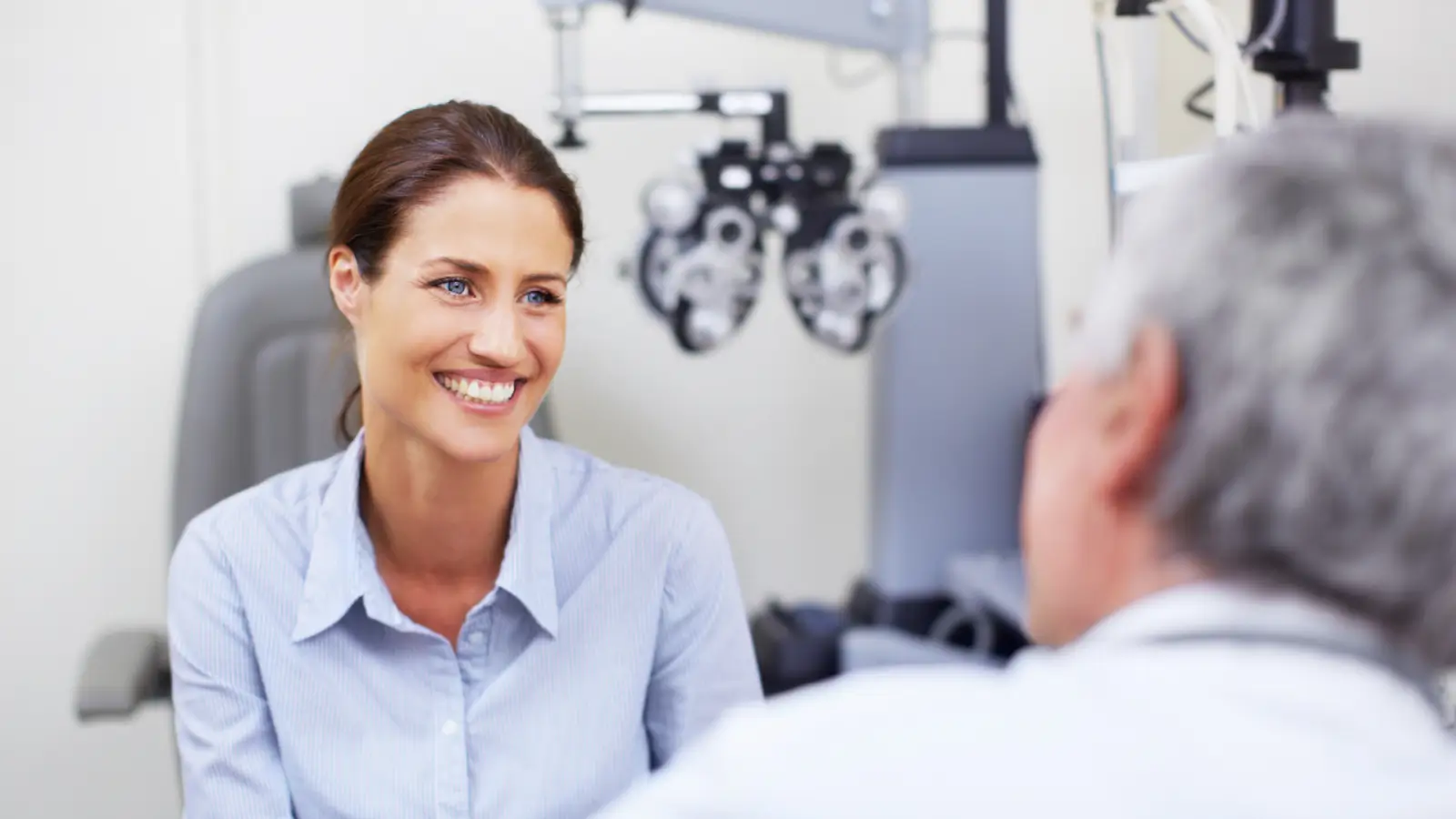 A woman in a light blue shirt smiles while discussing the Eylea success rate with an older man in a medical office. Equipment for eye examinations is visible in the background.